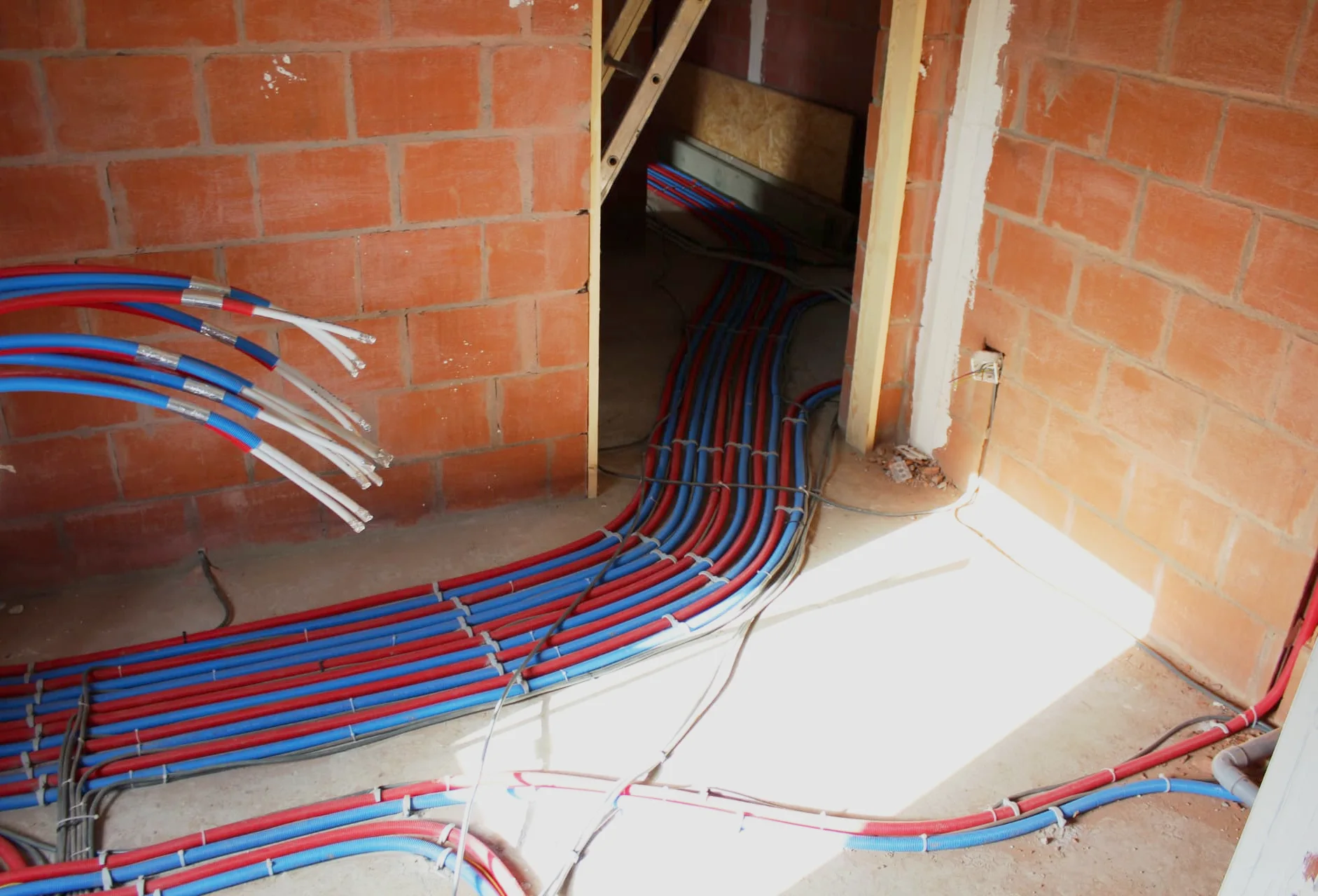 Tubes gainés rouge et bleu cheminant sur la dalle vers le couloir